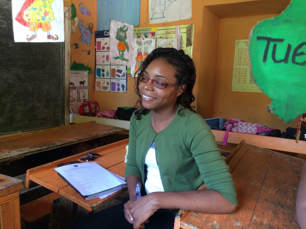 A teacher smiling away from the camera while sitting in one of the students' desks