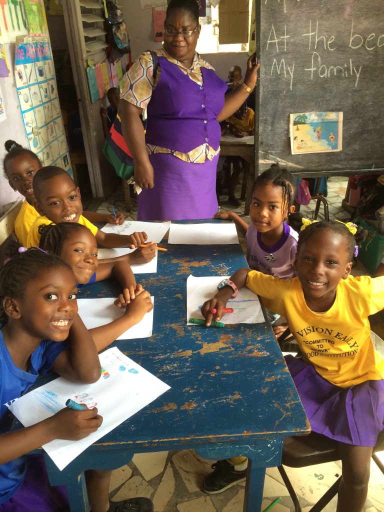 A Teacher with her class around a table working on sheets and smiling